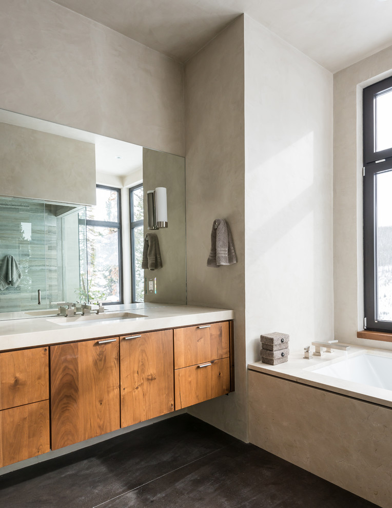 Modern inredning av ett badrum, med släta luckor, skåp i mörkt trä, ett undermonterat badkar, grå kakel, betonggolv och ett undermonterad handfat