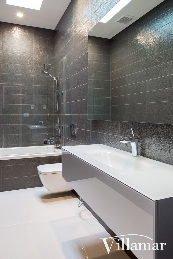 Design ideas for a medium sized modern bathroom in Vancouver with flat-panel cabinets, grey cabinets, a built-in bath, a shower/bath combination, a wall mounted toilet, grey tiles, ceramic tiles, grey walls, an integrated sink, engineered stone worktops and ceramic flooring.