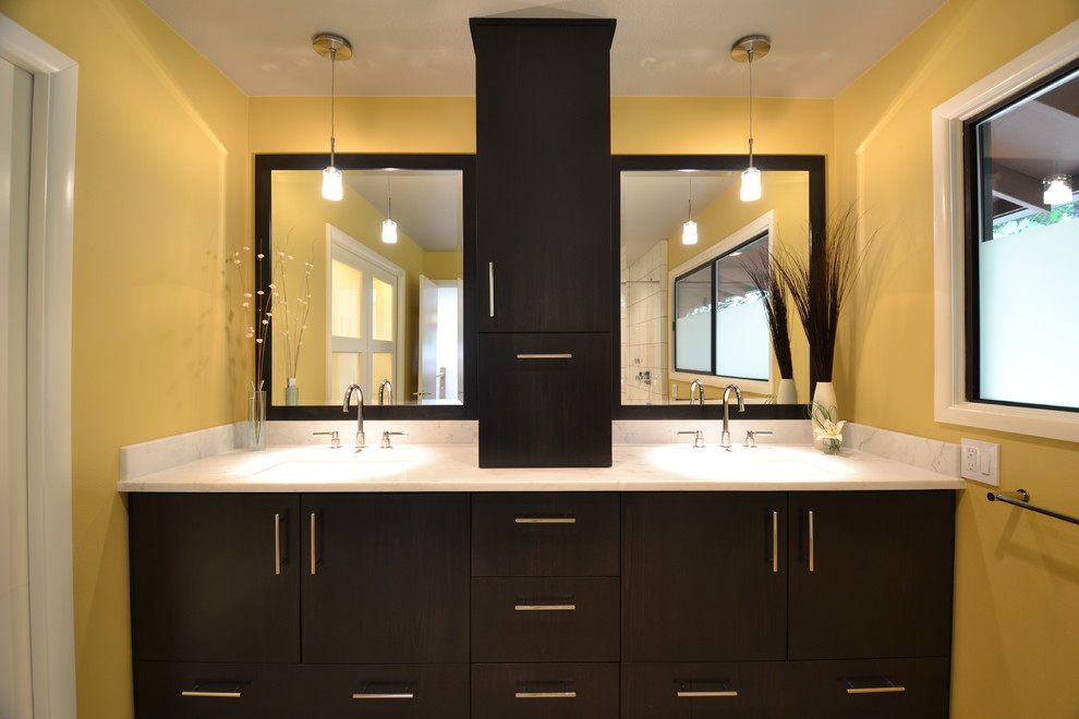 Cette photo montre une salle de bain principale moderne de taille moyenne avec un placard à porte plane, des portes de placard noires, un plan de toilette en marbre, un mur jaune et un lavabo encastré.