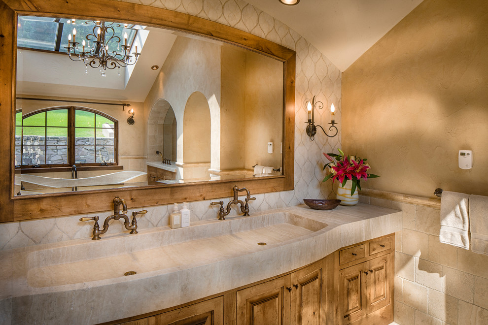 Bild på ett stort medelhavsstil en-suite badrum, med luckor med upphöjd panel, skåp i ljust trä, ett fristående badkar, beige kakel, stenkakel, beige väggar och ett integrerad handfat
