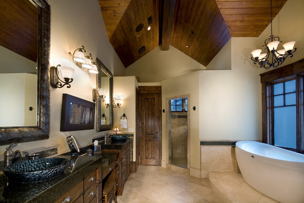 Large mountain style master beige tile and travertine tile travertine floor and beige floor bathroom photo in Salt Lake City with recessed-panel cabinets, dark wood cabinets, beige walls, a vessel sink, granite countertops and a hinged shower door
