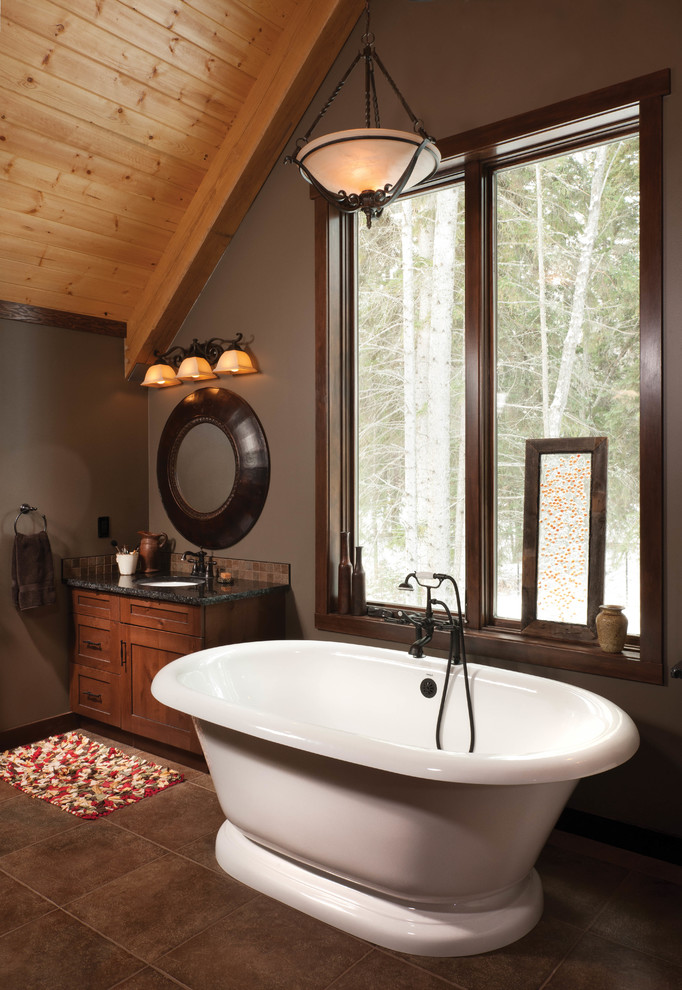 Cette photo montre une salle de bain principale montagne en bois brun de taille moyenne avec un lavabo encastré, un placard à porte shaker, un plan de toilette en granite, une baignoire indépendante, un carrelage marron et un mur gris.