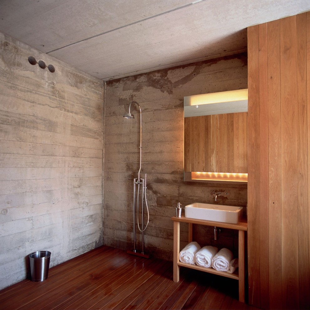 This is an example of a large rustic bathroom in New York with a console sink, light wood cabinets, wooden worktops, a walk-in shower, a wall mounted toilet, grey tiles, cement tiles, grey walls, dark hardwood flooring, an open shower and brown worktops.