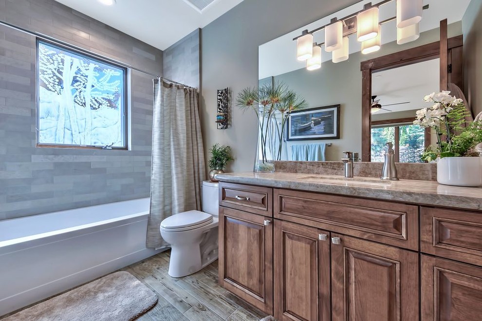 Bild på ett mellanstort vintage grå grått badrum med dusch, med luckor med upphöjd panel, skåp i mellenmörkt trä, en dusch/badkar-kombination, en toalettstol med hel cisternkåpa, grå kakel, porslinskakel, grå väggar, klinkergolv i porslin, ett undermonterad handfat, bänkskiva i kvartsit, flerfärgat golv och dusch med duschdraperi