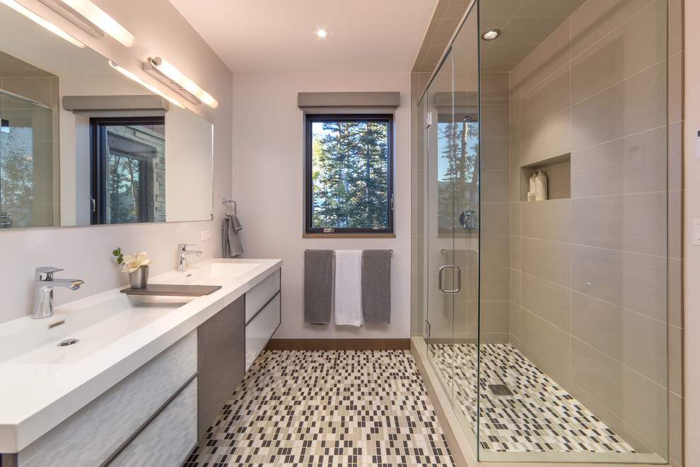 Modelo de cuarto de baño actual con lavabo de seno grande, armarios con paneles lisos, ducha esquinera, baldosas y/o azulejos grises, aseo y ducha y ventanas