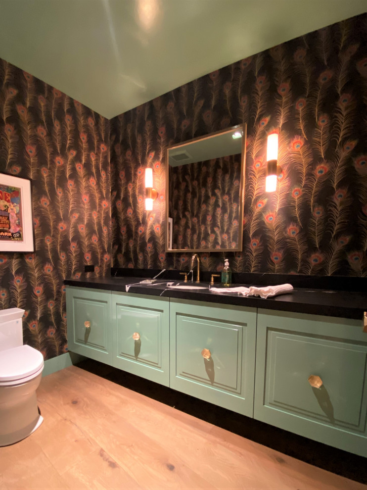 На фото: ванная комната среднего размера в стиле фьюжн с фасадами с выступающей филенкой, зелеными фасадами, раздельным унитазом, светлым паркетным полом, душевой кабиной, врезной раковиной, коричневым полом, черной столешницей, тумбой под одну раковину, подвесной тумбой и обоями на стенах