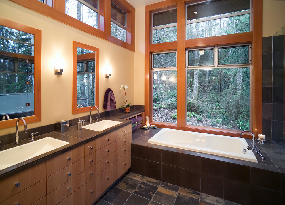 Trendy master slate floor bathroom photo in Seattle with a drop-in sink, flat-panel cabinets, light wood cabinets, tile countertops, a one-piece toilet and white walls