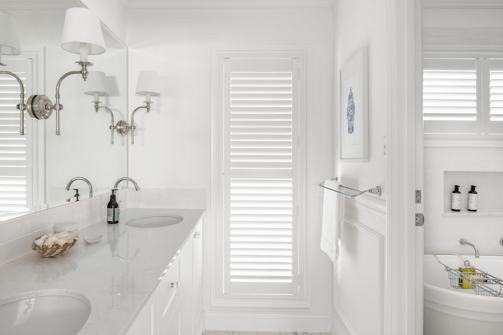 Photo of a medium sized coastal ensuite bathroom in Brisbane with shaker cabinets, white cabinets, a freestanding bath, white tiles, ceramic tiles, white walls, ceramic flooring, a submerged sink, engineered stone worktops, grey floors, white worktops, a wall niche, double sinks, a built in vanity unit and wainscoting.