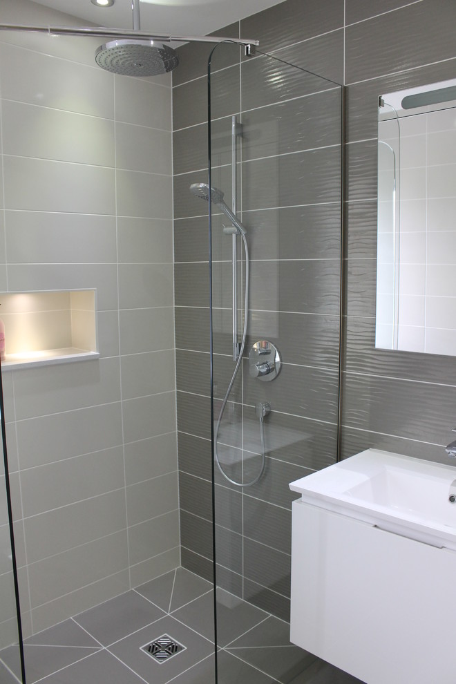 Foto på ett litet funkis badrum, med ett väggmonterat handfat, en vägghängd toalettstol, grå kakel och porslinskakel