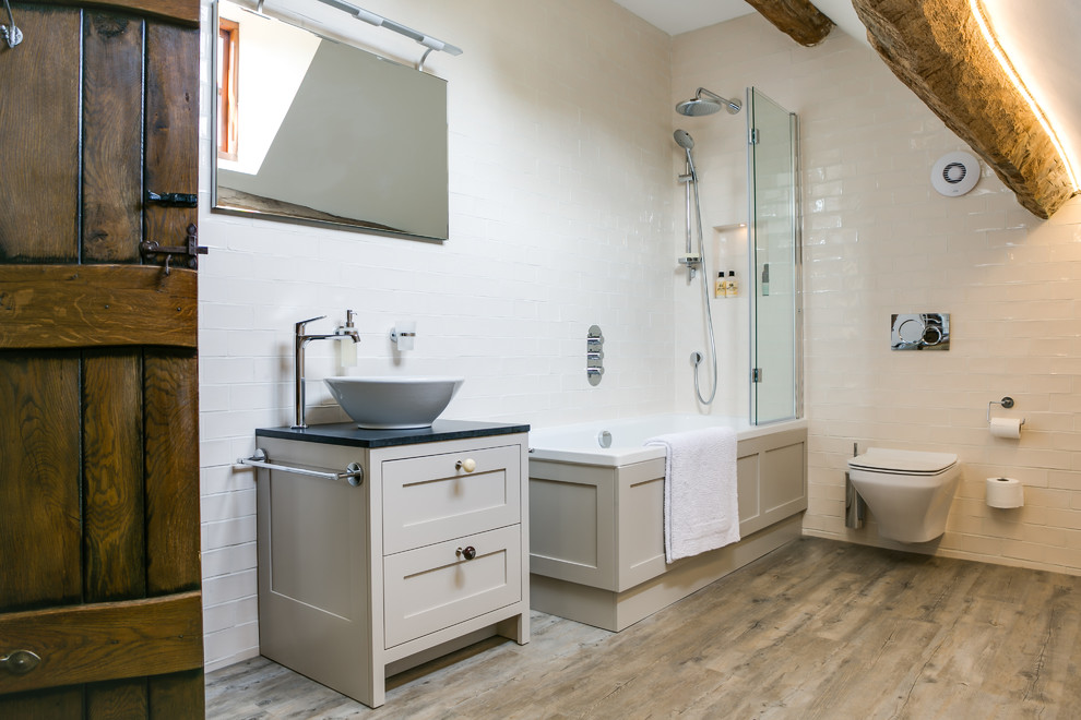 Mountain style white tile and subway tile bathroom photo in Gloucestershire with a vessel sink, recessed-panel cabinets, gray cabinets and a wall-mount toilet