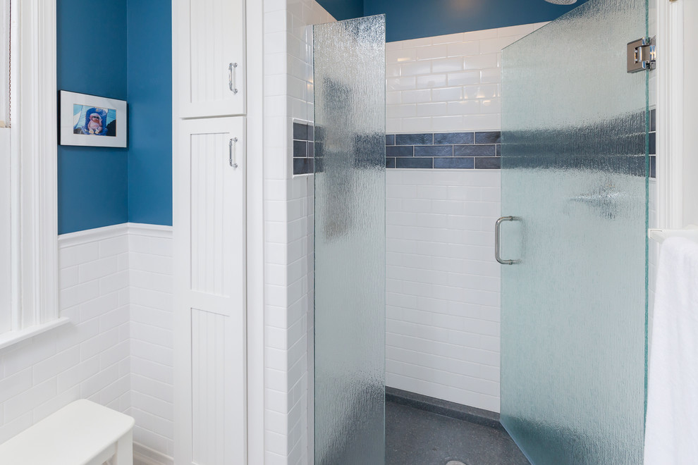 Modern inredning av ett mellanstort badrum med dusch, med en dusch i en alkov, en toalettstol med separat cisternkåpa, vit kakel, tunnelbanekakel, blå väggar, ett väggmonterat handfat, vitt golv och dusch med gångjärnsdörr