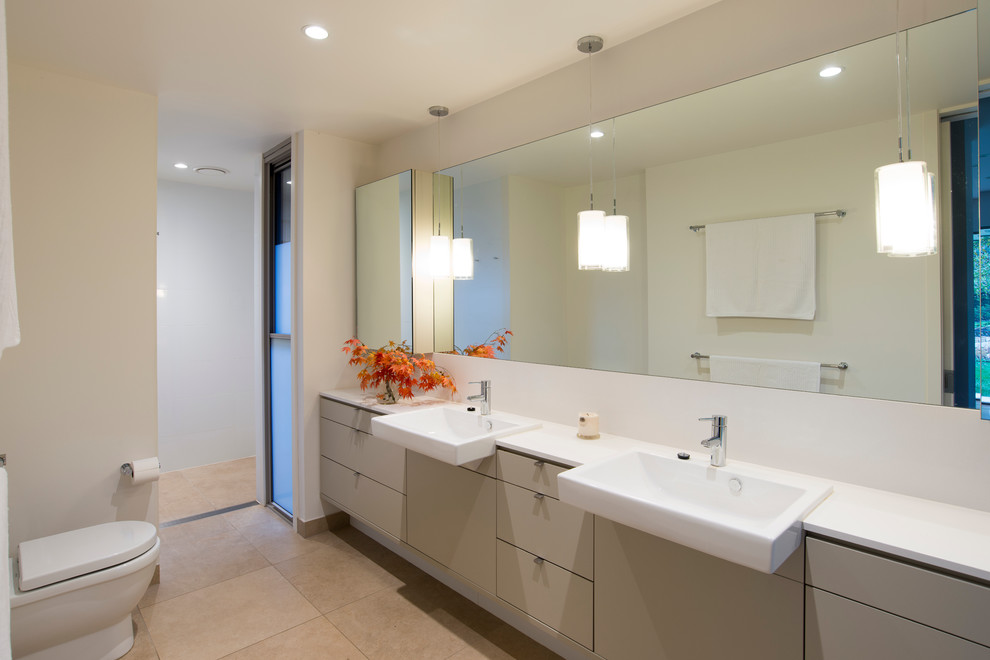 Cette photo montre une grande salle de bain principale tendance avec des portes de placard beiges, un plan de toilette en surface solide, un carrelage de pierre, une douche ouverte, WC à poser, un lavabo intégré et un mur blanc.