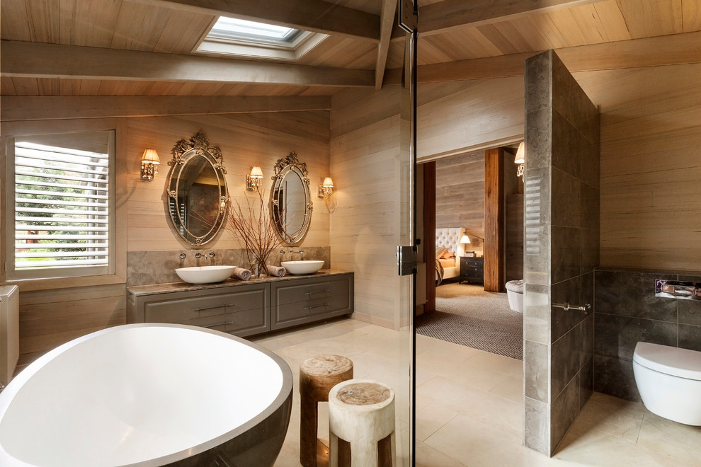 Cette image montre une salle de bain traditionnelle avec une vasque, un placard avec porte à panneau surélevé, des portes de placard marrons, une baignoire indépendante, WC suspendus et un carrelage marron.