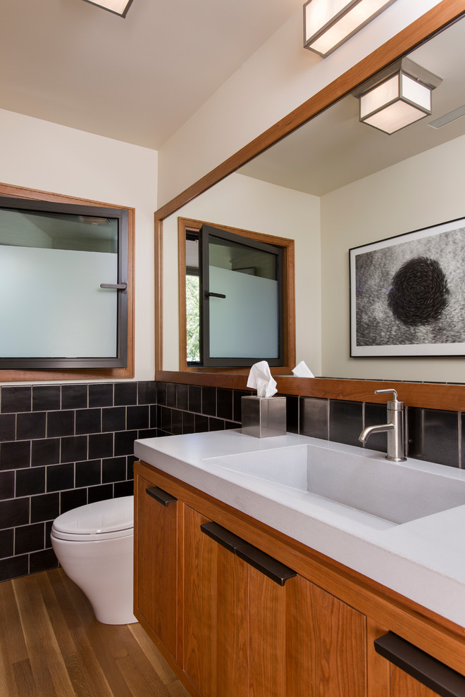 Photo of a small contemporary bathroom in Portland with flat-panel cabinets, medium wood cabinets, black tiles, ceramic tiles, light hardwood flooring and recycled glass worktops.
