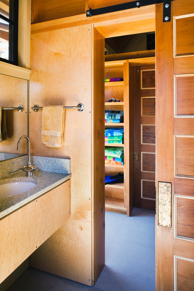 Cette image montre une petite salle de bain minimaliste en bois clair avec sol en béton ciré et un plan de toilette en verre recyclé.
