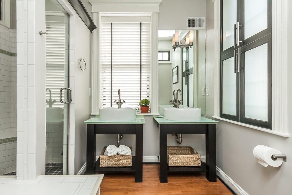 Modern inredning av ett badrum, med ett fristående handfat, öppna hyllor, bänkskiva i glas, en dusch i en alkov och vit kakel