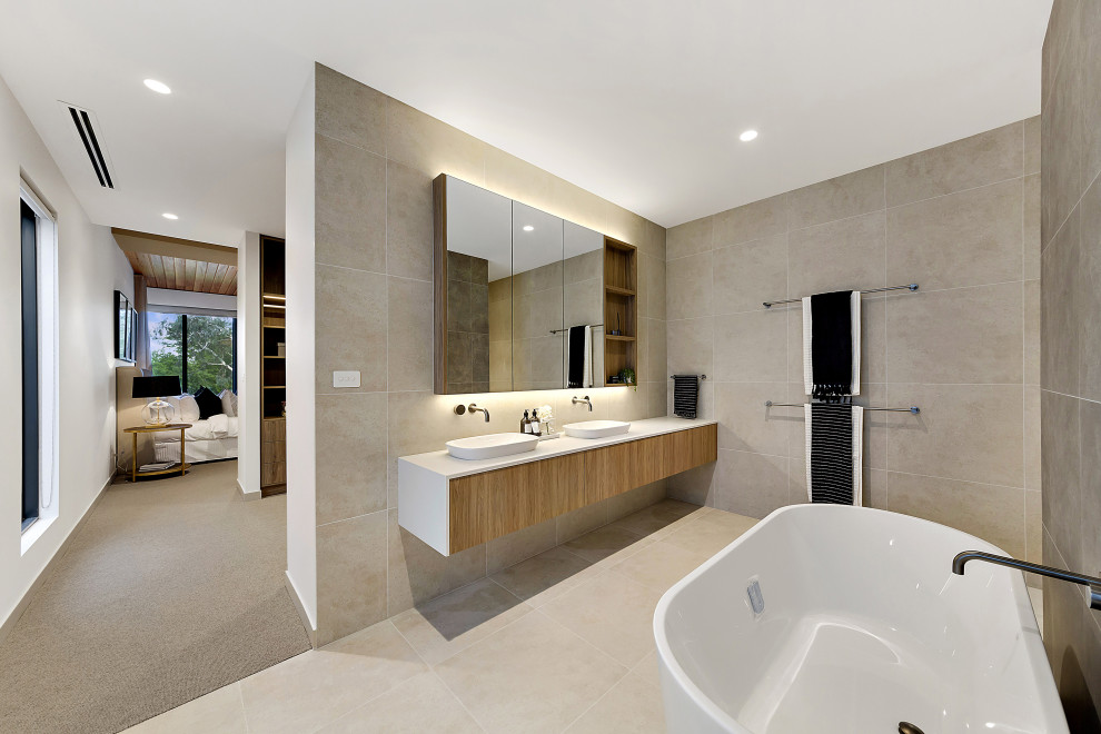 Inredning av ett modernt stort vit vitt en-suite badrum, med släta luckor, skåp i mellenmörkt trä, ett fristående badkar, en öppen dusch, grå kakel, porslinskakel, grå väggar, klinkergolv i porslin, ett fristående handfat, bänkskiva i kvarts, grått golv och med dusch som är öppen