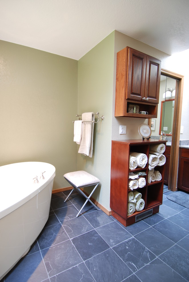 Idée de décoration pour une grande salle de bain principale design en bois brun avec un placard avec porte à panneau surélevé, une baignoire indépendante, un carrelage gris, un carrelage de pierre, un mur vert et un sol en ardoise.