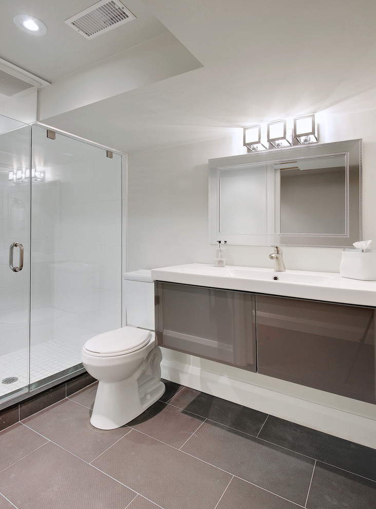 Amerikansk inredning av ett litet badrum med dusch, med ett integrerad handfat, släta luckor, grå skåp, bänkskiva i akrylsten, en dusch i en alkov, en toalettstol med separat cisternkåpa, grå kakel, porslinskakel, beige väggar och klinkergolv i porslin