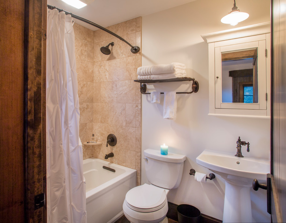 Inredning av ett litet badrum, med en dusch/badkar-kombination, mellanmörkt trägolv, ett piedestal handfat och dusch med duschdraperi