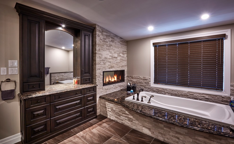 This is an example of a large traditional ensuite bathroom in Toronto with raised-panel cabinets, dark wood cabinets, an alcove bath, a two-piece toilet, beige tiles, stone tiles, beige walls, porcelain flooring, a submerged sink, granite worktops and brown floors.
