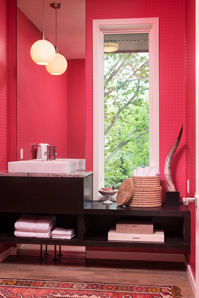 Exemple d'une salle de bain chic avec une vasque, un placard sans porte, des portes de placard marrons, un plan de toilette en granite, un mur rose et un sol en bois brun.