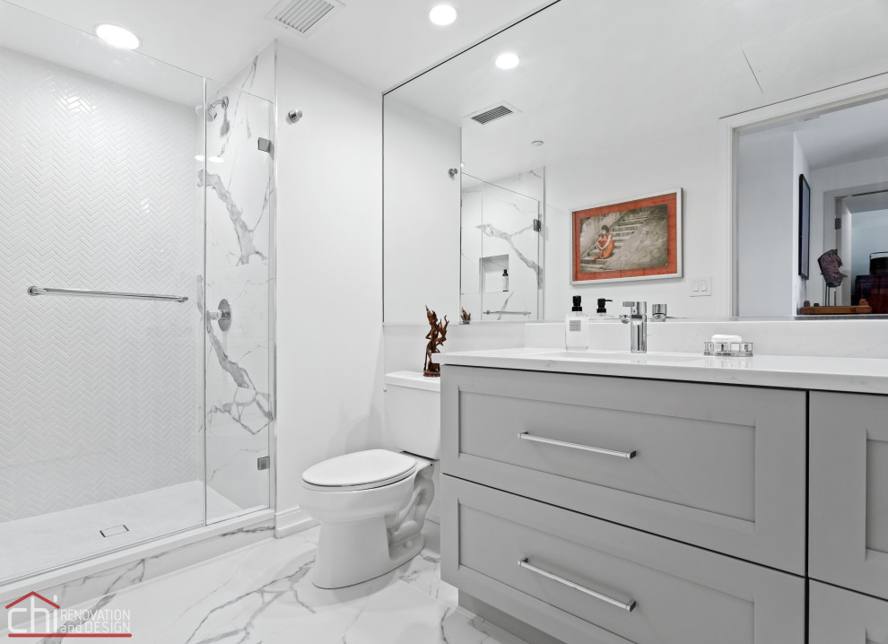 Photo of a large contemporary ensuite bathroom in Chicago with black cabinets, a freestanding bath, a one-piece toilet, grey tiles, cement tiles, grey walls, marble flooring, a submerged sink, engineered stone worktops, white floors, white worktops, double sinks and a built in vanity unit.