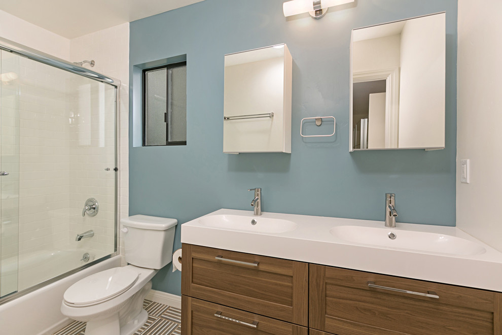 Example of a mid-sized trendy master white tile and ceramic tile ceramic tile and multicolored floor bathroom design in San Diego with shaker cabinets, brown cabinets, a two-piece toilet, blue walls, an integrated sink, solid surface countertops and white countertops