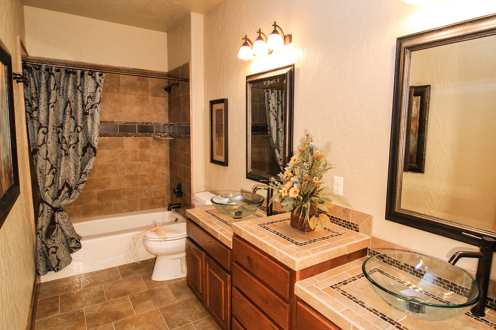 Photo of a large rustic family bathroom in Seattle with a vessel sink, raised-panel cabinets, medium wood cabinets, tiled worktops, a built-in bath, a shower/bath combination, a two-piece toilet, beige tiles, ceramic tiles, beige walls and ceramic flooring.