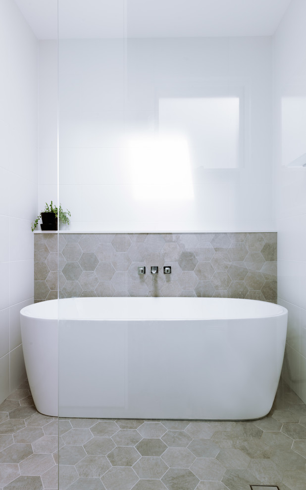 Inredning av ett modernt mellanstort vit vitt en-suite badrum, med släta luckor, skåp i ljust trä, ett fristående badkar, en öppen dusch, en toalettstol med hel cisternkåpa, vit kakel, tunnelbanekakel, vita väggar, klinkergolv i porslin, ett väggmonterat handfat, bänkskiva i kvarts, grått golv och med dusch som är öppen