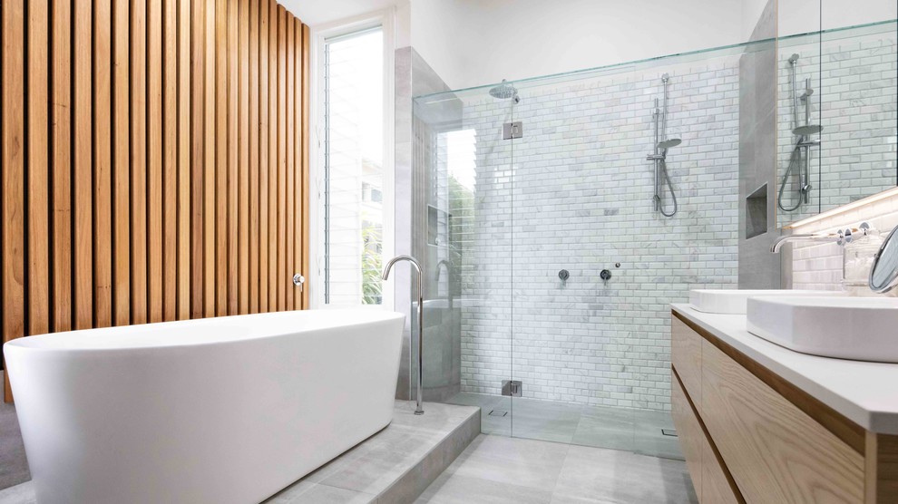 Large contemporary ensuite bathroom in Melbourne with freestanding cabinets, light wood cabinets, a built-in bath, a double shower, a wall mounted toilet, white tiles, marble tiles, white walls, cement flooring, engineered stone worktops, grey floors and a shower curtain.
