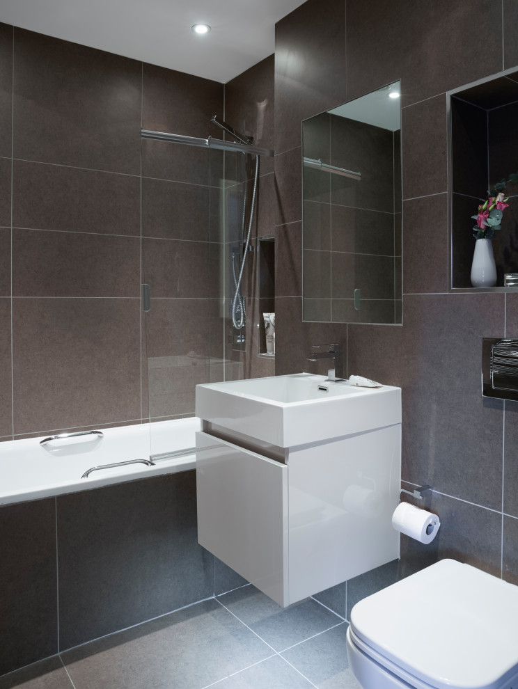 Design ideas for a small modern family bathroom in London with flat-panel cabinets, white cabinets, an alcove bath, a shower/bath combination, a one-piece toilet, brown tiles, ceramic tiles, brown walls, ceramic flooring, engineered stone worktops, brown floors and white worktops.