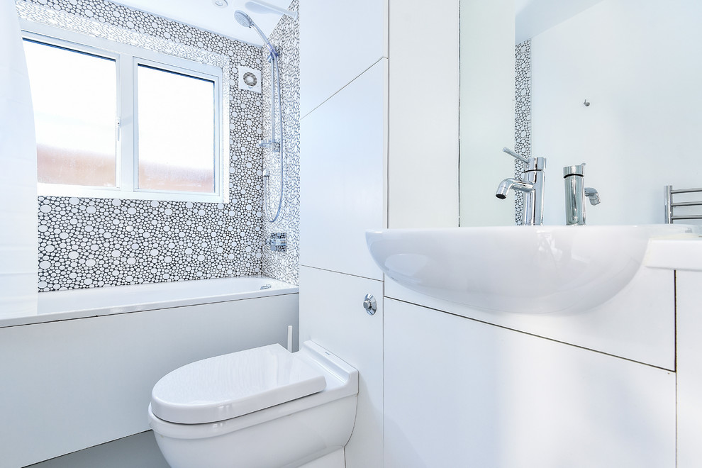 Design ideas for a small contemporary family bathroom in London with flat-panel cabinets, white cabinets, a built-in bath, a built-in shower, a one-piece toilet, white tiles, ceramic tiles, white walls, lino flooring, an integrated sink, laminate worktops, grey floors, a shower curtain and white worktops.