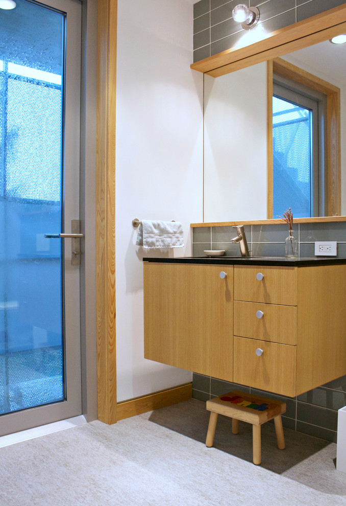 Inspiration för ett funkis badrum med dusch, med släta luckor, skåp i ljust trä, grå kakel, glaskakel och vita väggar