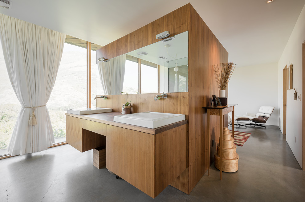 Modern inredning av ett badrum, med släta luckor, skåp i mellenmörkt trä, vita väggar, betonggolv och ett fristående handfat