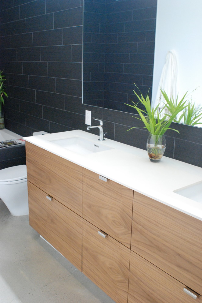 Cette image montre une douche en alcôve minimaliste en bois brun avec un placard à porte plane, une baignoire encastrée, WC à poser, un carrelage noir, des carreaux de porcelaine et un lavabo encastré.