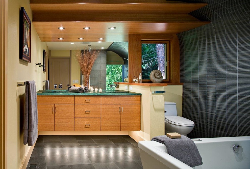 Cette image montre une grande salle de bain principale asiatique en bois brun avec un placard à porte plane, une baignoire indépendante, WC séparés, un carrelage noir, un carrelage bleu, un carrelage gris, des carreaux en allumettes, un mur jaune, un sol en ardoise, un lavabo encastré, un plan de toilette en granite et un plan de toilette vert.