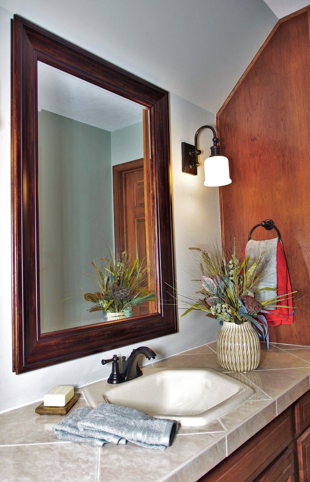 Cette photo montre une douche en alcôve chic en bois brun avec un lavabo intégré, un placard avec porte à panneau encastré, un plan de toilette en carrelage, une baignoire en alcôve, WC à poser, un carrelage beige, un mur gris et un sol en bois brun.