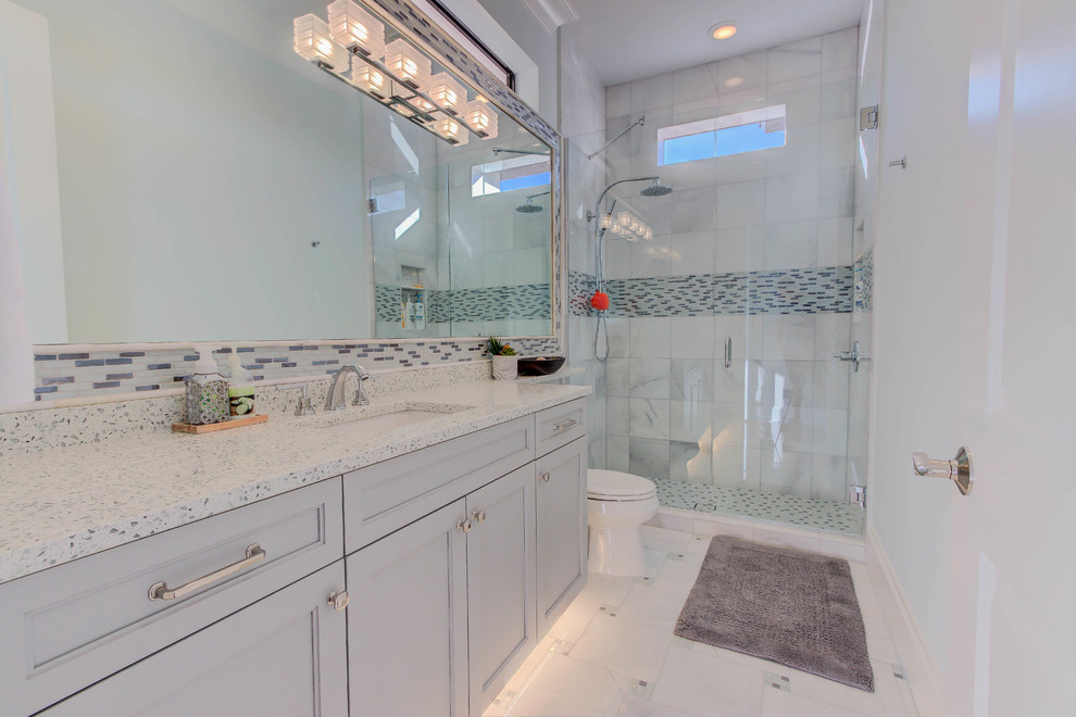 Idées déco pour une salle de bain contemporaine de taille moyenne avec un placard à porte shaker, des portes de placard grises, une douche ouverte, WC séparés, un carrelage blanc, des carreaux de porcelaine, un mur bleu, un sol en carrelage de porcelaine, un lavabo encastré, un plan de toilette en verre recyclé, un sol blanc et une cabine de douche à porte battante.