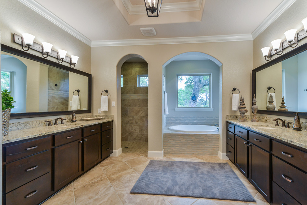 Photo of a large classic ensuite bathroom in Austin with a submerged sink, shaker cabinets, dark wood cabinets, granite worktops, a built-in bath, a walk-in shower, a two-piece toilet, beige tiles, porcelain tiles, beige walls, porcelain flooring, brown floors and an open shower.