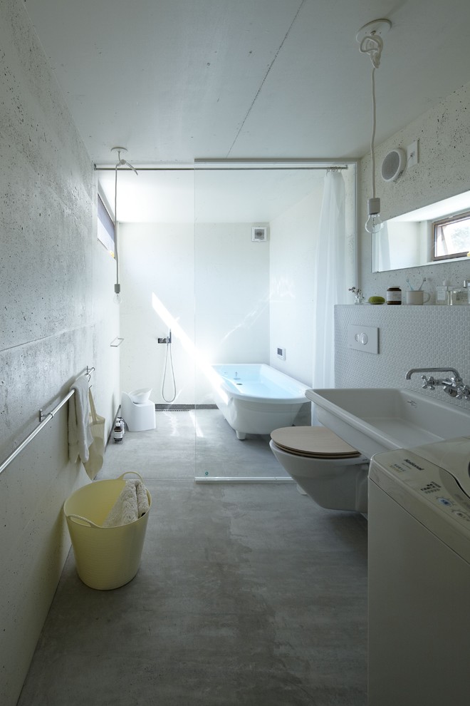 Cette image montre une salle de bain minimaliste avec un lavabo suspendu, WC suspendus, sol en béton ciré et une cabine de douche avec un rideau.