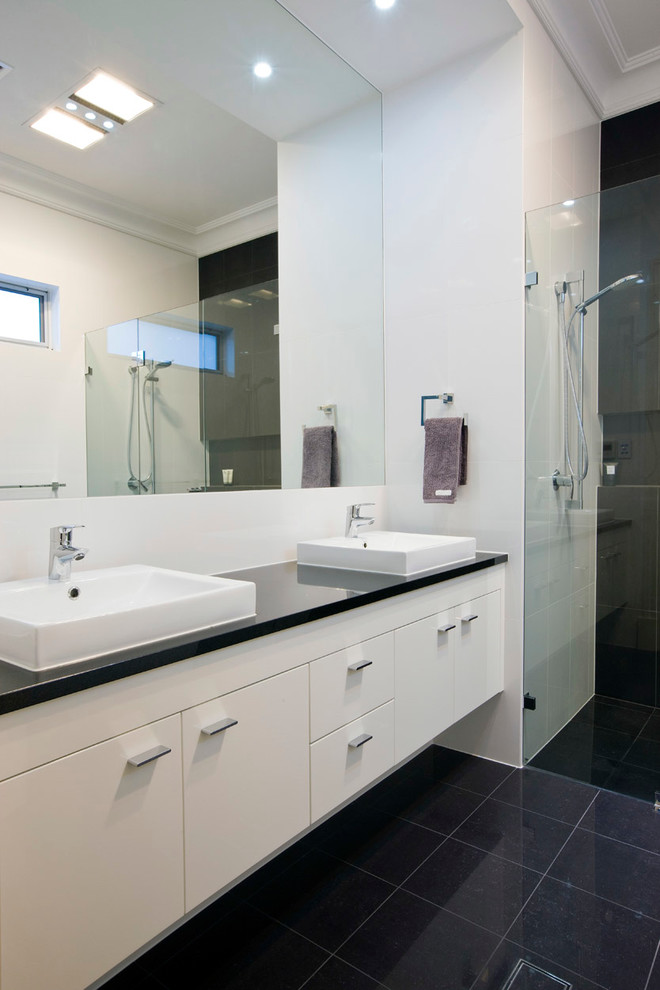アデレードにあるコンテンポラリースタイルのおしゃれな浴室 (ベッセル式洗面器、フラットパネル扉のキャビネット、白いキャビネット、バリアフリー、黒いタイル、白い壁) の写真
