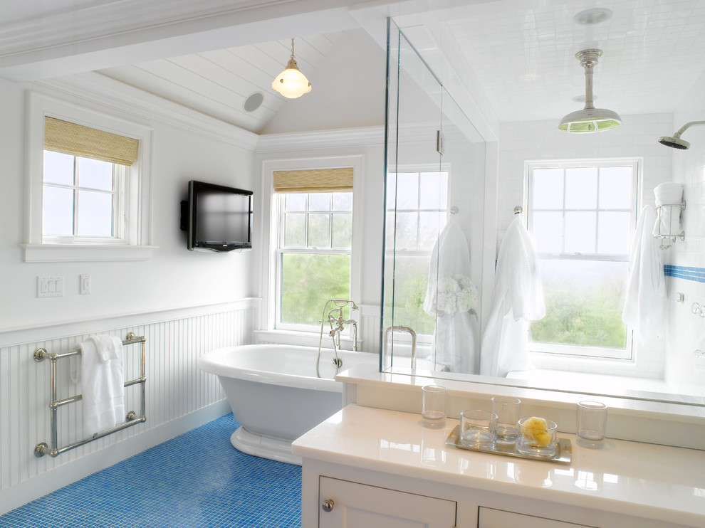 Foto på ett maritimt badrum, med ett fristående badkar, en hörndusch, luckor med infälld panel, vita skåp, vit kakel, mosaikgolv och blått golv