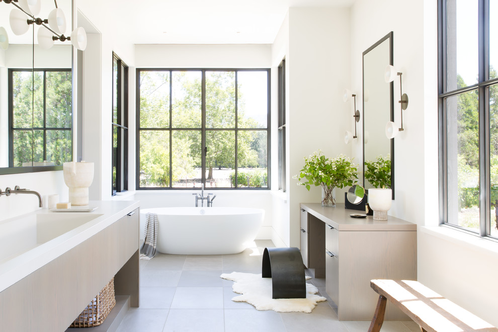Foto på ett lantligt vit badrum, med släta luckor, skåp i ljust trä, ett fristående badkar, vita väggar, ett integrerad handfat och grått golv