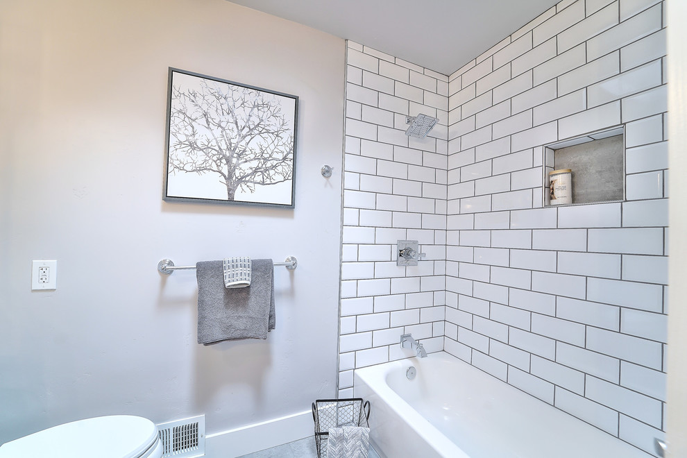 Exempel på ett mellanstort lantligt badrum för barn, med möbel-liknande, skåp i slitet trä, en dusch/badkar-kombination, en toalettstol med separat cisternkåpa, vit kakel, keramikplattor, grå väggar, klinkergolv i porslin, ett undermonterad handfat, marmorbänkskiva och brunt golv