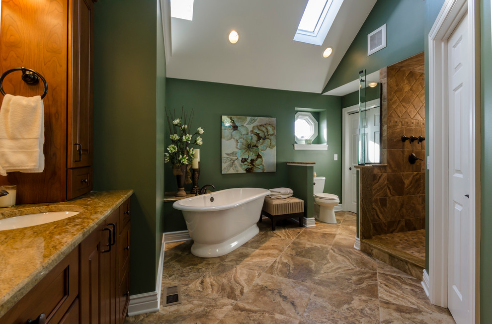 Inredning av ett klassiskt mycket stort en-suite badrum, med ett undermonterad handfat, luckor med upphöjd panel, skåp i mellenmörkt trä, granitbänkskiva, ett fristående badkar, en öppen dusch, en toalettstol med separat cisternkåpa, brun kakel, porslinskakel, gröna väggar och klinkergolv i porslin