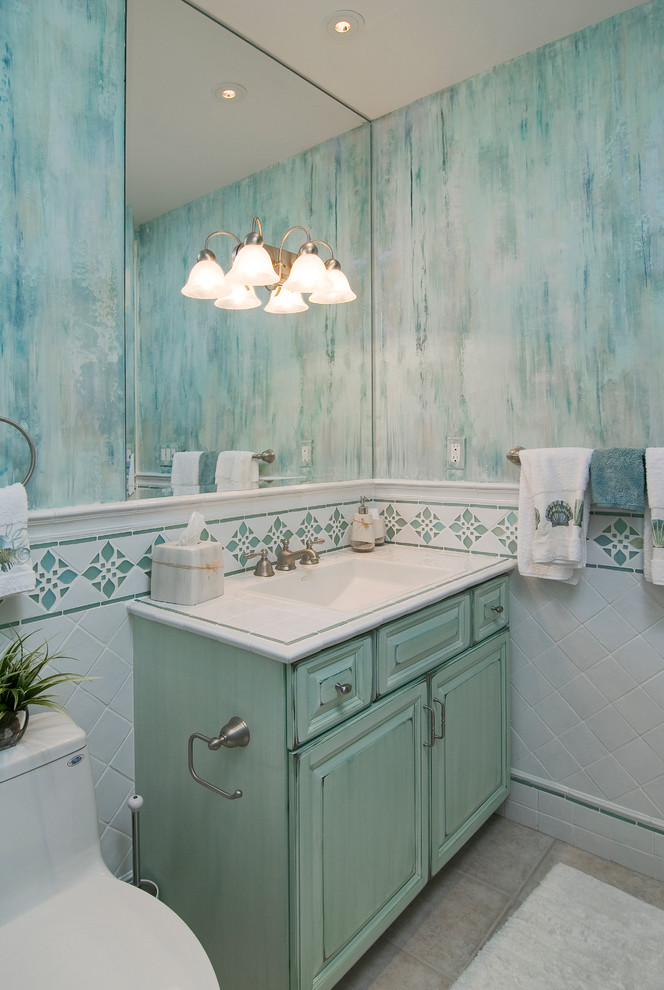 Maritimes Badezimmer mit integriertem Waschbecken, Schränken im Used-Look, gefliestem Waschtisch, Toilette mit Aufsatzspülkasten, weißen Fliesen, Porzellanfliesen, bunten Wänden und Porzellan-Bodenfliesen in Miami