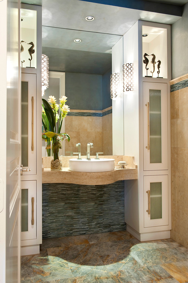 This is an example of a traditional bathroom in Miami with a vessel sink, glass-front cabinets, white cabinets, beige tiles and grey walls.