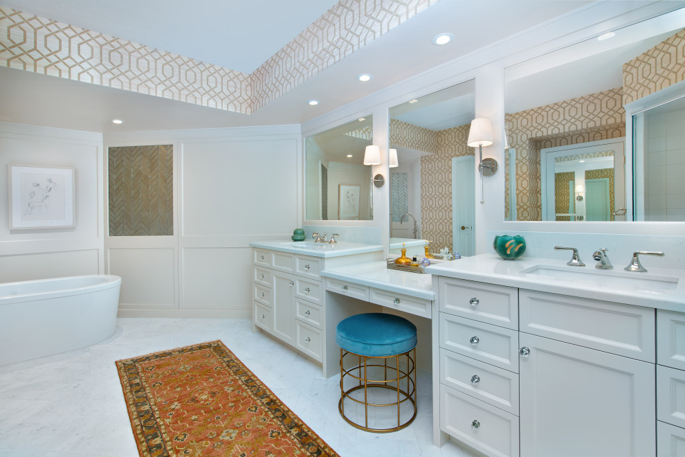 Inspiration for a medium sized classic ensuite bathroom in Chicago with recessed-panel cabinets, white cabinets, a freestanding bath, mirror tiles, beige walls, marble flooring, a submerged sink, engineered stone worktops, white floors, white worktops, double sinks, a built in vanity unit and wallpapered walls.