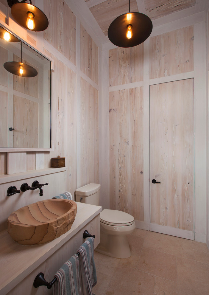 Foto på ett tropiskt badrum, med ett fristående handfat, öppna hyllor, skåp i slitet trä, beige kakel och stenkakel